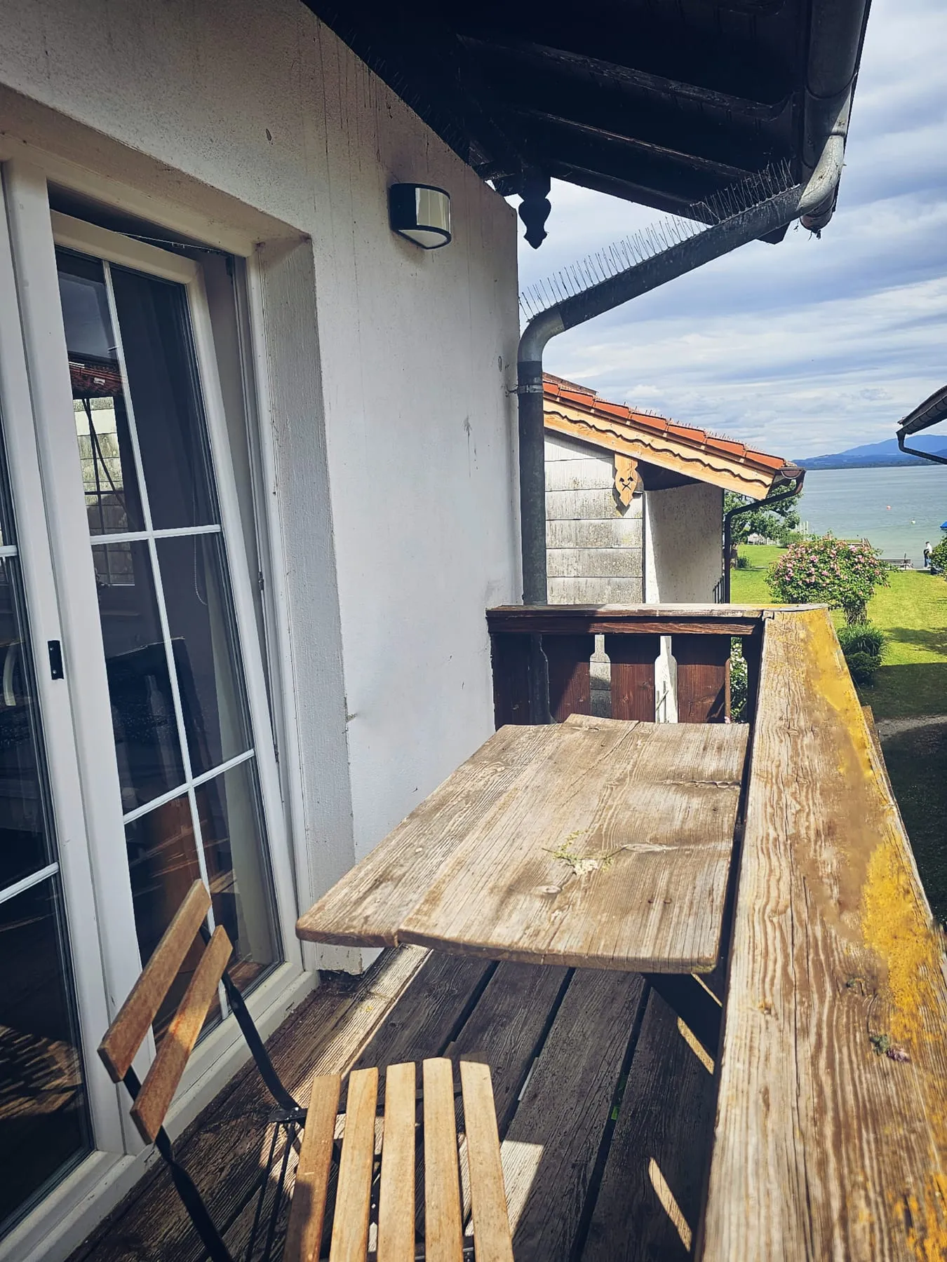 Sonniger Balkon mit Holztisch und Blick in den grünen Garten